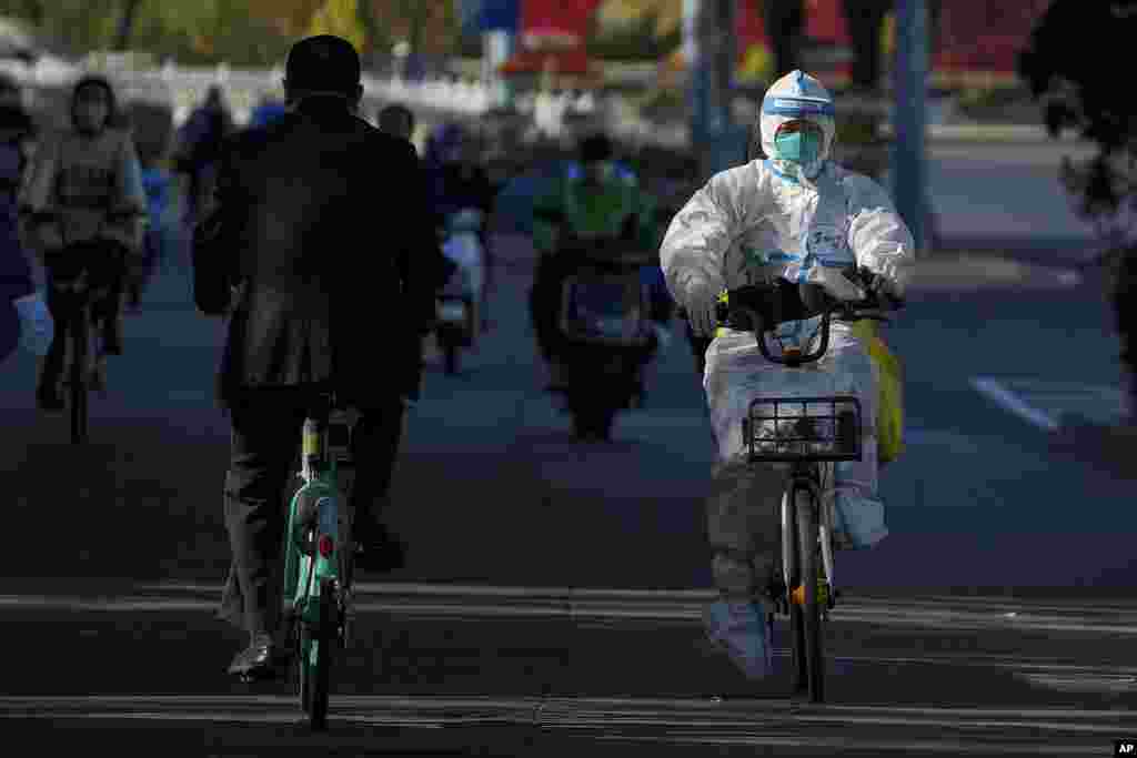 A worker in protective gear rides on a street as she heads to take COVID-19 samples from residents who have been under home quarantine in Beijing. The ruling Communist Party is enforcing a "Zero COVID" policy that has closed areas throughout China for weeks to try to isolate every case. 