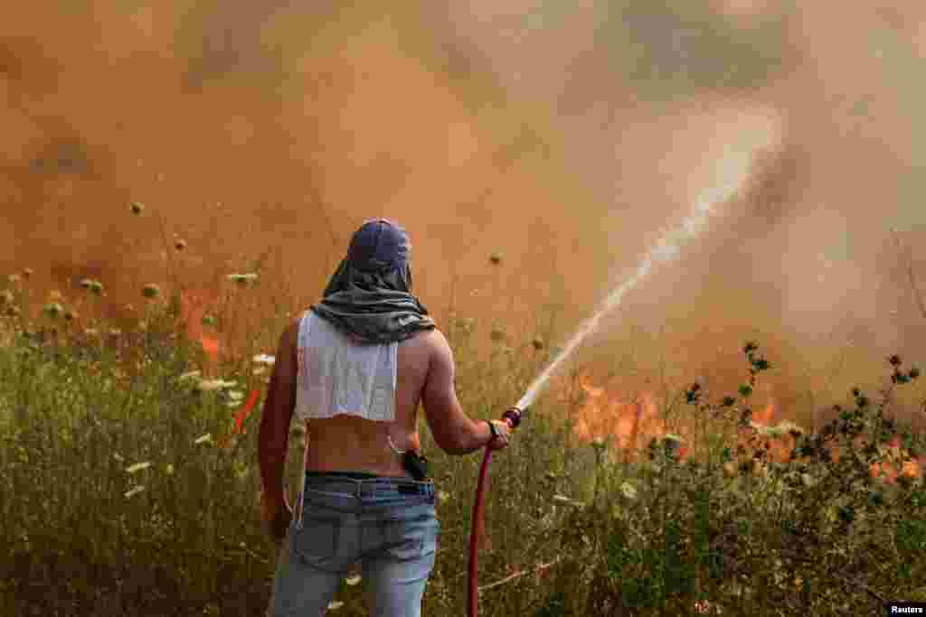 An Israeli man extinguishes a fire following rocket attacks from Lebanon, amid ongoing cross-border hostilities between Hezbollah and Israeli forces, in Katzrin in the Israeli-occupied Golan Heights.