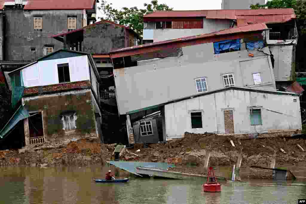 A woman on a boat looks at damaged houses on the banks of Cau River in Vietnam&#39;s Bac Ninh province.