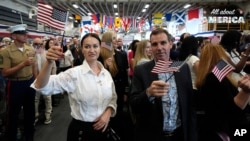 Novi američki državljani Reni Ivanova i njen suprug Nasko Ivanov iz Bugarske mašu američkim zastavicama tokom ceremonije naturalizacije u Majamiju, 7. maja 2024. godine. (Foto: AP/Lynne Sladky)