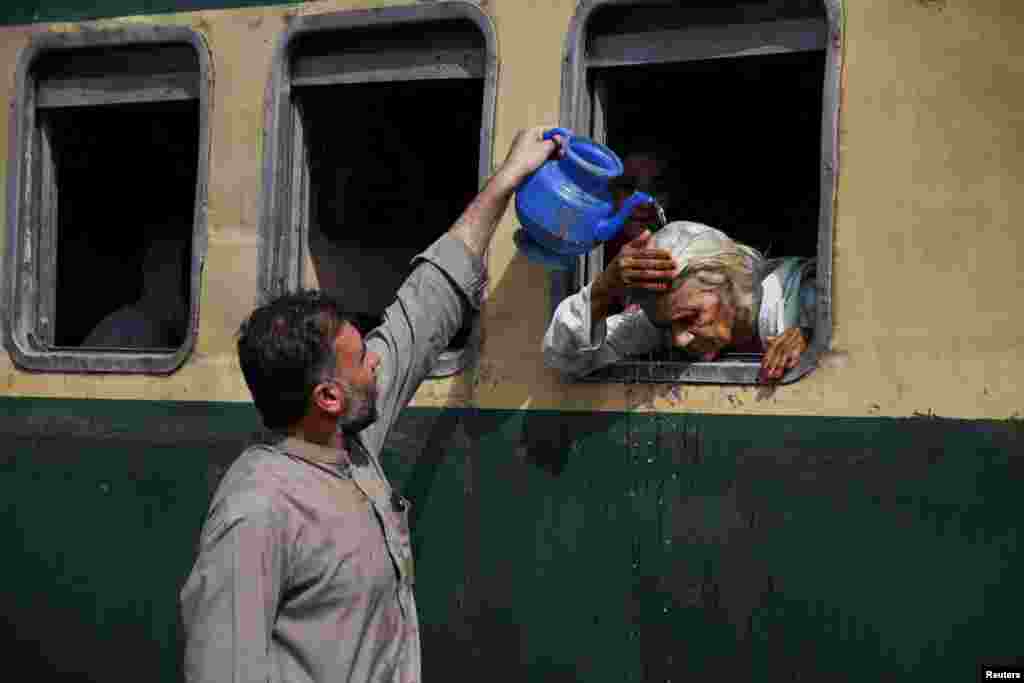 A man pours water on a passenger's head to cool off during a hot and humid day at the Hyderabad Railway Station in Hyderabad, Pakistan.