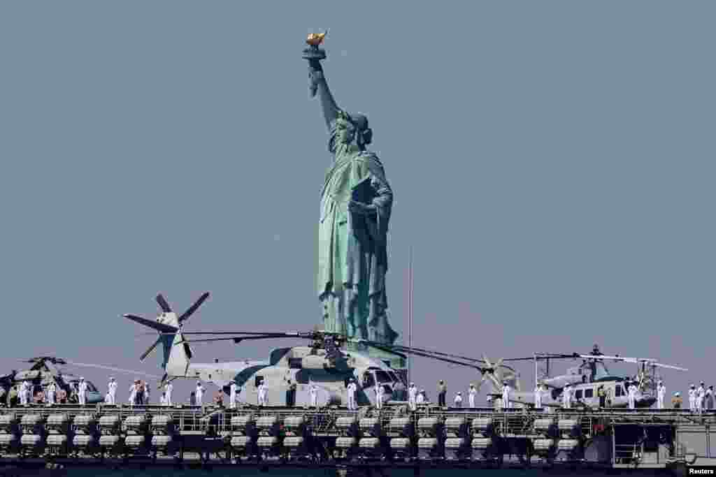 Sailors and Marines line the deck of the USS Bataan (LHD-5) Wasp-class amphibious assault ship, as it passes by the Statue of Liberty arriving in New York Harbor during the parade of ships to kick off "Fleet Week 2024” in New York City.