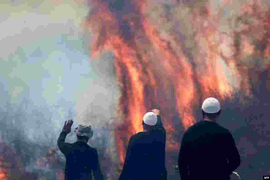 Local Druze men watch the flames burning a field after rockets launched from southern Lebanon landed on the Banias area in the Israel-annexed Golan Heights amid ongoing cross-border clashes between Israeli troops and Hezbollah fighters.