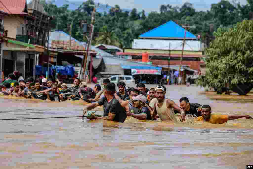 People holding a rope wade through flood water after the Kobe River overflowed following heavy rains in Lukulamo, North Maluku, Indonesia.