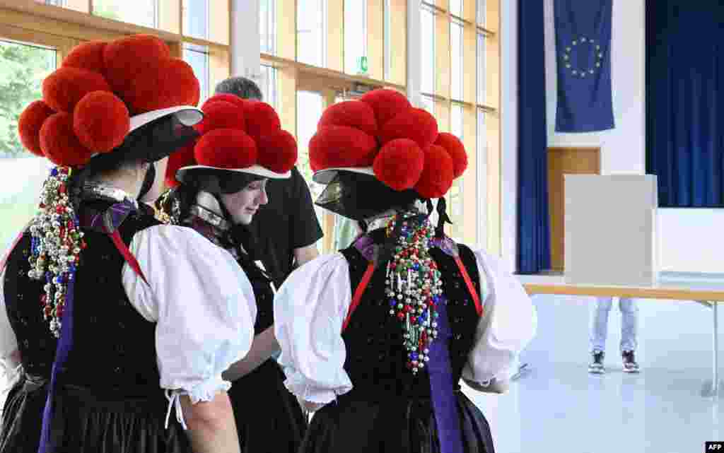 Women wearing traditional "Bollenhut" pompon hats, typical for the Black Forest region, line up to fill out their ballot papers for European Parliament Elections at a polling station in Gutach, southern Germany.