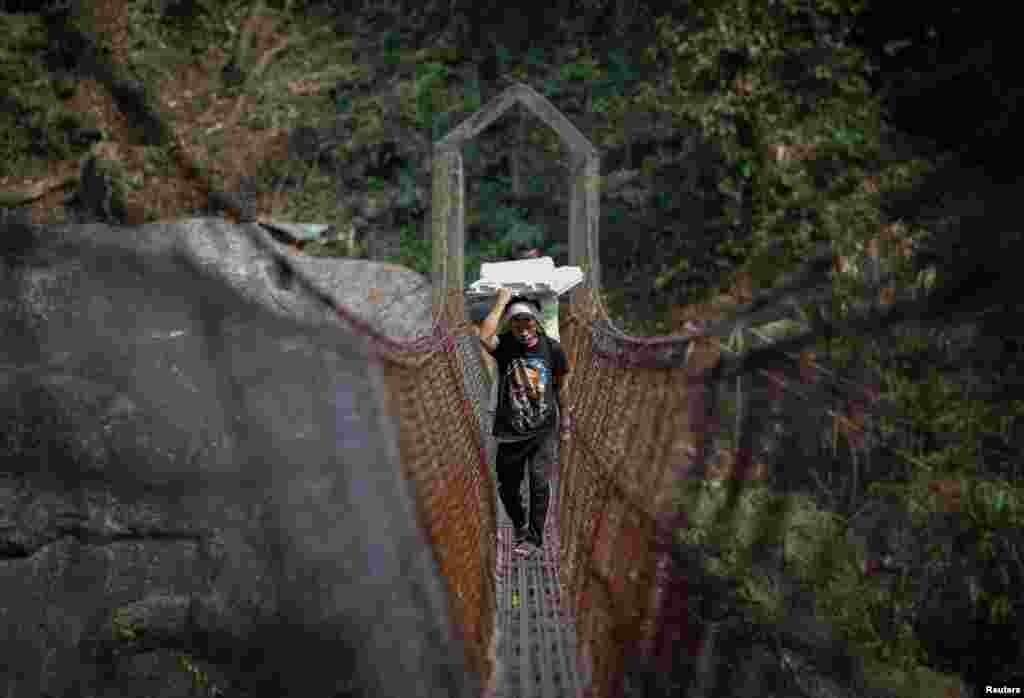 Cornelius Mawa, 28, a porter, carries Voter Verifiable Paper Audit Trail and Electronic Voting Machines as he crosses a suspension bridge to reach a remote polling station in Shillong in the northeastern state of Meghalaya, India, April 17, 2024.