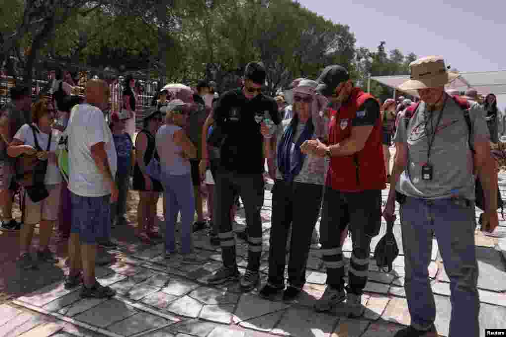 A woman is aided outside the Acropolis hill archaeological site after feeling unwell, as a heatwave hits Athens, Greece.