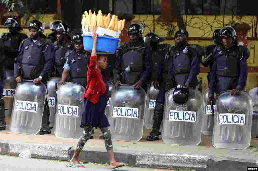 A woman walks past police officers as Angola's election commission says ruling MPLA party leads with 52% majority, after the general election close in Luanda.