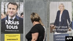 Peatones pasan frente a carteles de campaña del presidente francés y el candidato a la reelección Emmanuel Macron (izquierda) y la candidata presidencial de la extrema derecha Marine Le Pen en Eguisheim, este de Francia, el 21 de abril de 2022.