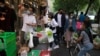 2022年4月25日，新冠肺炎疫情爆发后，戴着防护口罩的人们在商店外的摊位上购买蔬菜。