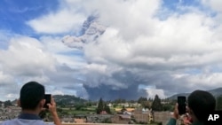 Men use their mobile phones to take photos as Mount Sinabung spews volcanic materials into the air as it erupts, in Karo, North Sumatra, Indonesia, Aug. 10, 2020.