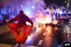 Seorang penggemar memegang bendera Maroko ketika skuter listrik terbakar di bagian belakang di sela-sela siaran langsung pertandingan sepak bola Grup F Piala Dunia 2022 Qatar antara Belgia dan Maroko, di Brussel, pada 27 November 2022. (Foto: AFP)
