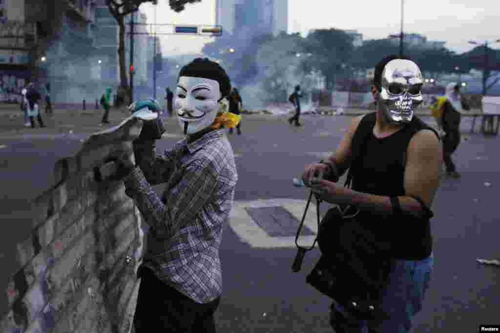 Anti-government demonstrators wearing masks hold a makeshift shield during clashes with police at Altamira square in Caracas, Feb. 27, 2014.