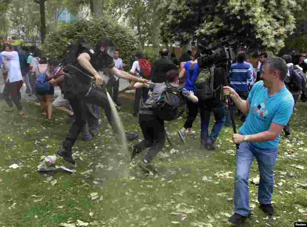 Seorang polisi anti huru-hara Turki menggunakan gas air mata untuk membubarkan protes terhadap penghancuran pohon di sebuah taman yang dilakukan untuk pembangunan jalan kaki lima, di Lapangan Taksim di Istanbul, Turki.