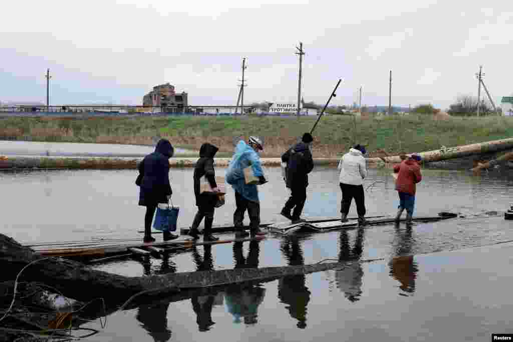 People return to their shelters as they cross a destroyed bridge after collecting aid, as Russia's invasion of Ukraine continues, in the eastern Donbas region of Bakhmut, Ukraine, Oct. 30, 2022. 