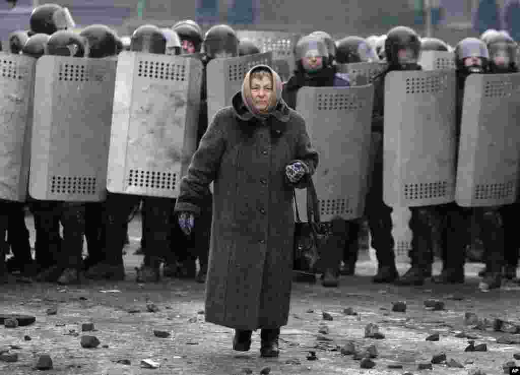A woman walks from police officers as they block a street during unrest in central Kyiv, Jan. 21, 2014.