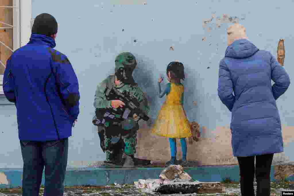 People look at an artwork of the famous street artist Tvboy, created on a wall of the House of Culture, which was heavily damaged during Russia&#39;s attack on Ukraine, in the town of Irpin, outside Kyiv.