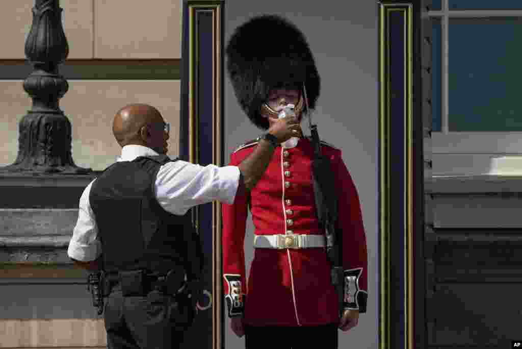 A police officer givers water to a British soldier wearing a traditional bearskin hat, on guard duty outside Buckingham Palace, during hot weather in London.