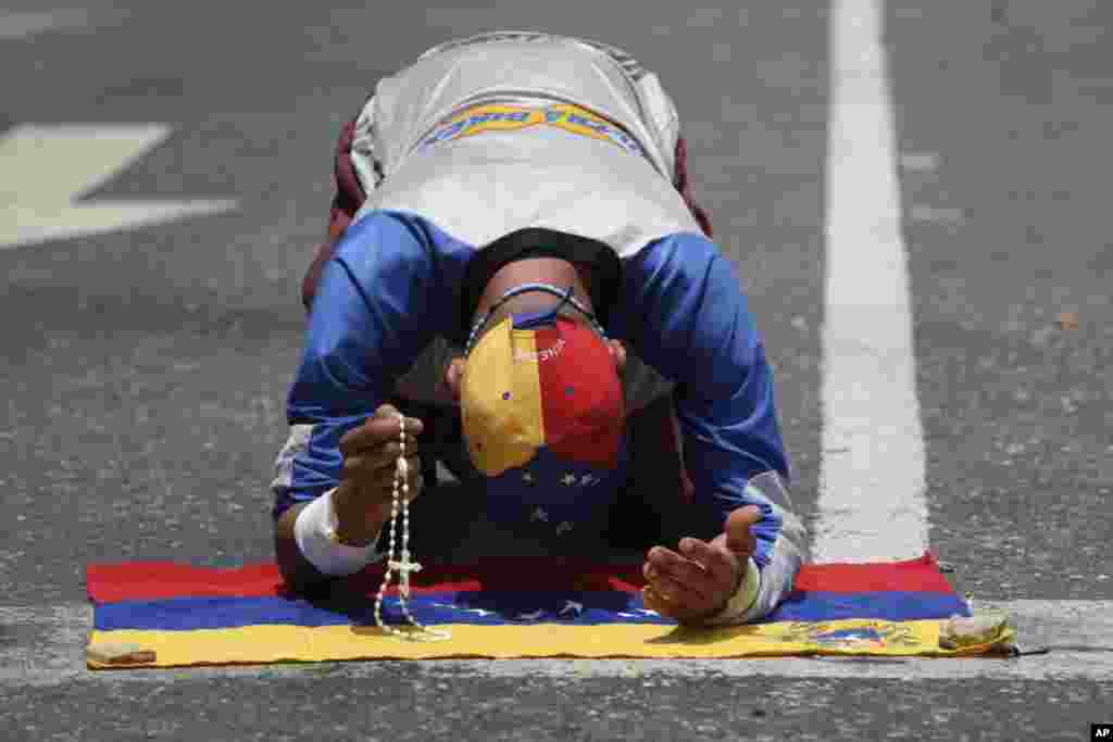A demonstrator holding a rosary prays over a Venezuelan flag prior to a march against the government of President Nicolas Maduro in Caracas, Venezuela.