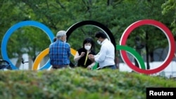 路人在坐落在日本奥委会总部附近的奥运五环徽标前闲谈。（路透社2021年6月23日照片）