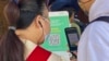 一名香港市民(白衣者)正准备使用防疫手机应用程式“安心出行”进入一间餐厅用膳，身旁的餐厅职员检视使用者是否有准确扫瞄餐厅入口的二维码 (美国之音/汤惠芸)