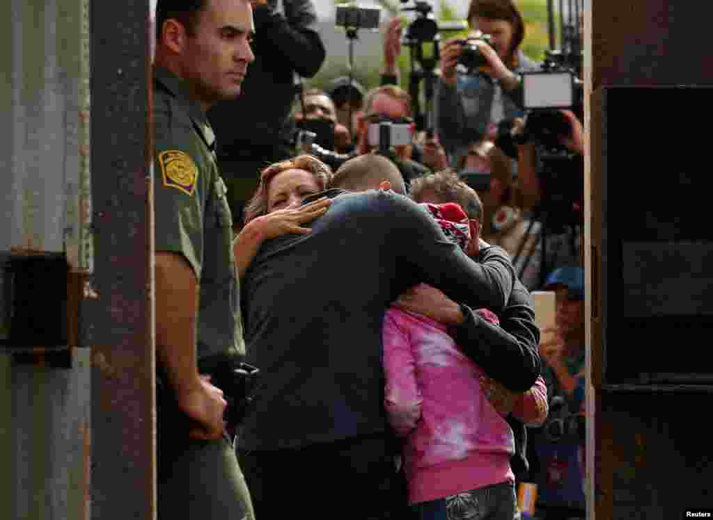 Penjaga perbatasan AS siaga sementara Adrian Gonzalez-Morales (warga AS) dan putrinya Aileen memeluk orang tua Adrian, Juan and Martha (warga Meksiko), di perbatasan AS-Meksiko di California.