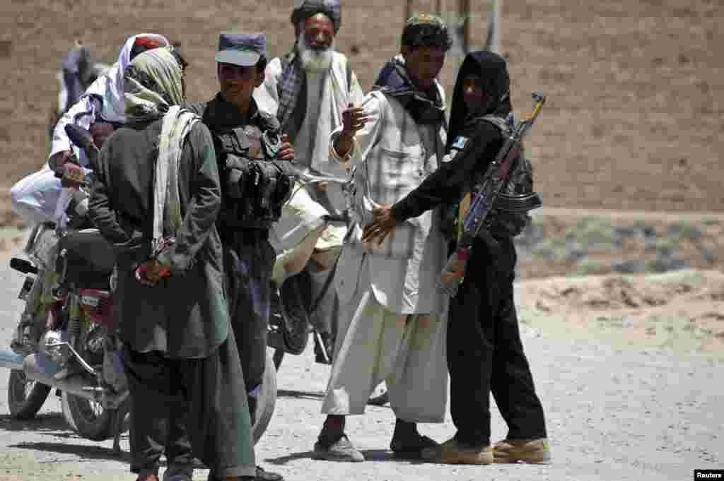 Afghan policemen search people near the house belonging to Afghan President Hamid Karzai's cousin, Hashmat Karzai, at the site of a suicide attack, in Kandahar, July 29, 2014.