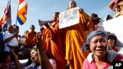 Cambodian land eviction victims and Buddhist monks shout slogans during a rally in front of the National Assembly in Phnom Penh, Cambodia, Friday, Nov. 14, 2014. They demanded to released land activists who were arrested during a protest against flooding and activists who were arrested during a protest against the jailing of land activists. (AP Photo/Heng Sinith)