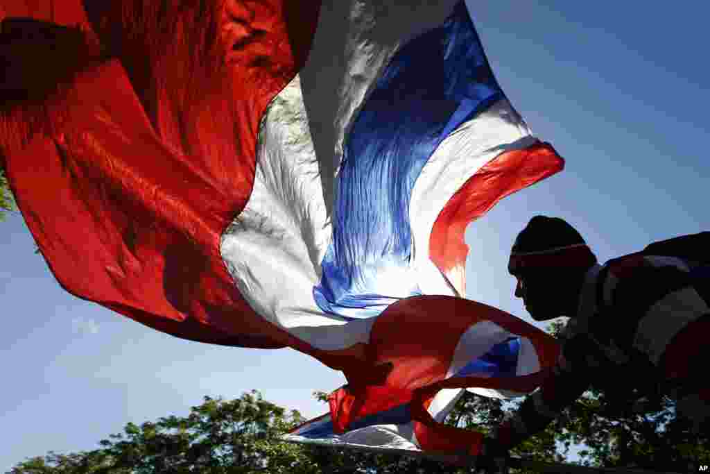 Seorang pengunjuk rasa anti-pemerintah melambaikan bendera nasional Thailand ketika terjadi unjuk rasa di pusat kota Bangkok. Komisi anti korupsi negara itu mendakwa perdana menteri yang digulingkan Yingluck Shinawatra pada hari Kamis atas tuduhan kelalaian dalam tugas mengawasi program subsidi beras yang mendapat kecaman luas. 