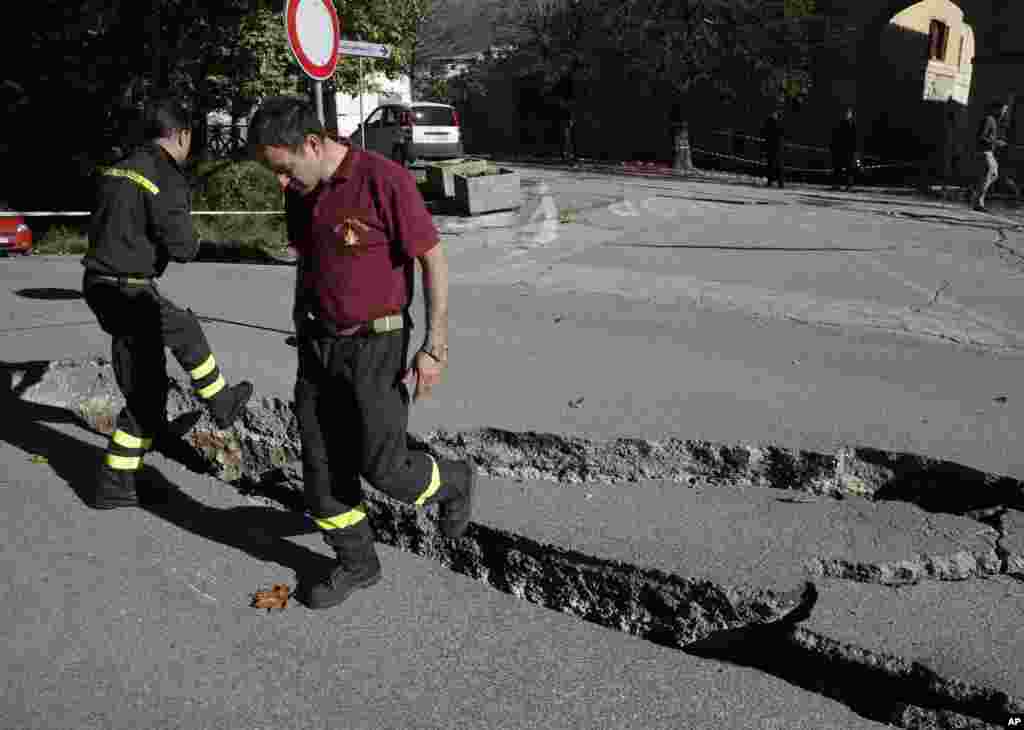 Petugas pemadam kebakaran memeriksa retakan di jalan akibat gempa di Norcia, Italia tengah (30/10). (AP/Gregorio Borgia)