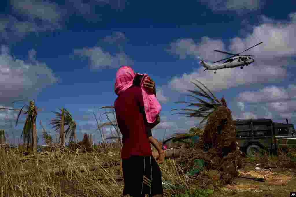 Seorang korban topan Haiyan yang selamat menggendong anaknya yang dibungkus dengan handuk sambil melihat helikopter yang mendarat membawa bantuan ke kota Guiuan yang hancur, di Pulau Samar, Filipina.