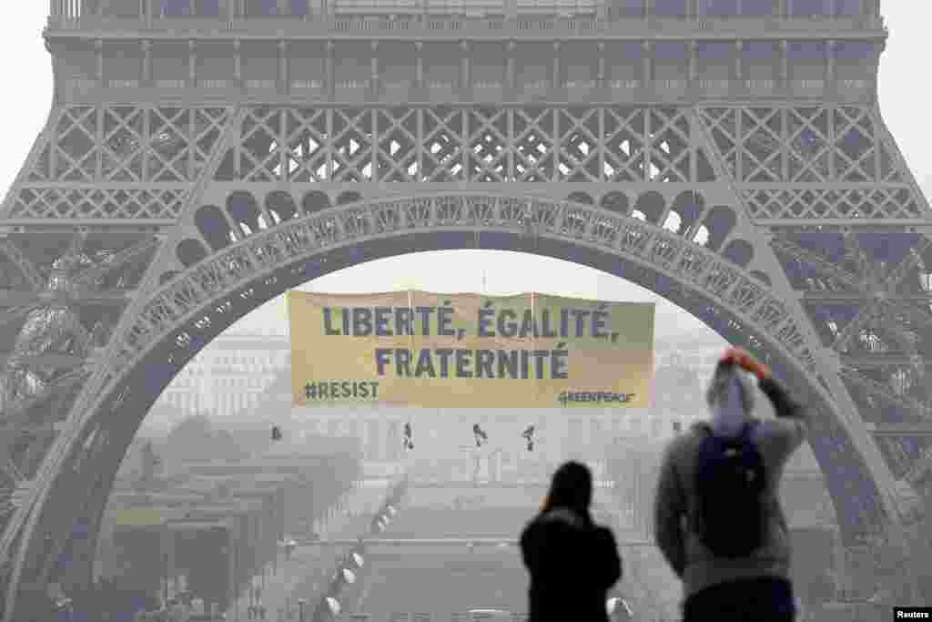 Para turis berjalan di alun-alun Trocadero saat para aktivis dari kelompok lingkungan Greenpeace membentangkan spanduk raksasa di Menara Eiffel yang bertuliskan "Liberty, Equality, Fraternity" dalam sebuah seruan pada warga negara Prancis untuk memberikan suara melawan calon presiden Front Nasional Marine Le Pen, di Paris.