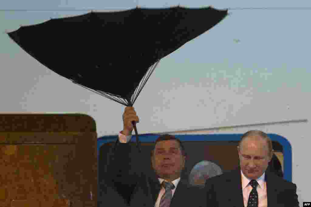Seorang anggota Paspampres Rusia kesulitan mengembangkan payung, sementara Presiden Vladimir Putin keluar dari pesawat dalam kunjungan di Shanghai, China.