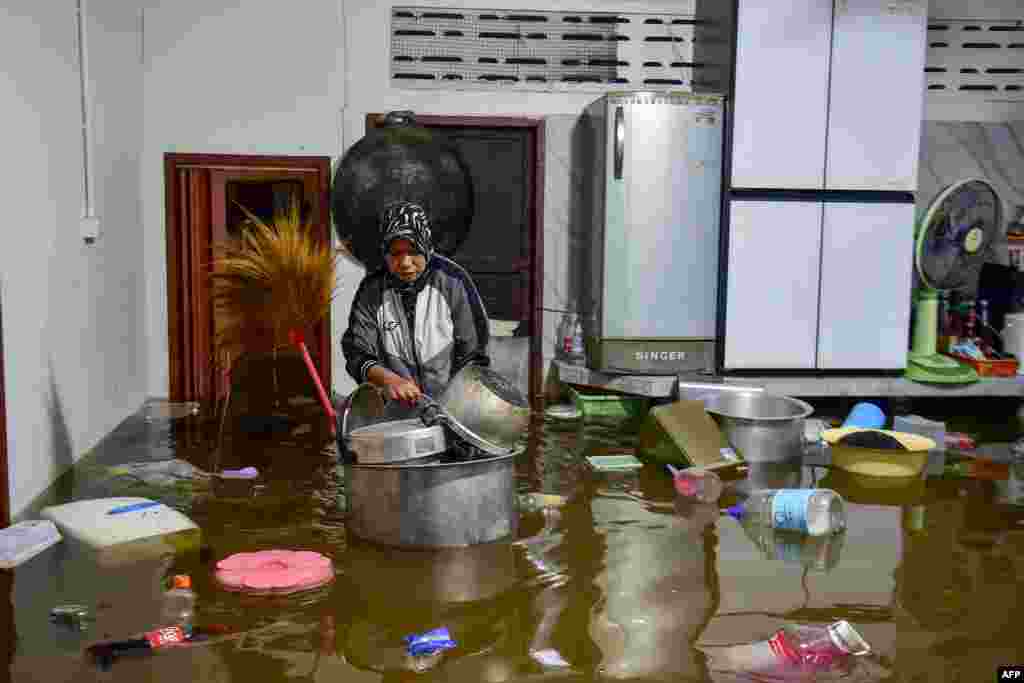 A resident looks pots floating in flood waters inside her kitchen following heavy rain in Thailand's southern province of Narathiwat.