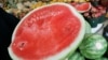 A person holds a cut watermelon at a fruit stand. 