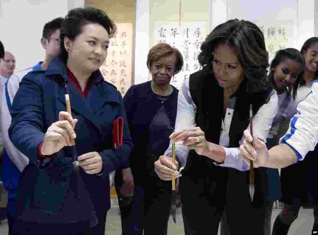 中国国家主席习近平的夫人彭丽媛3月21日向美国第一夫人米歇尔.奥巴马展示如何使用毛笔，当时她们在参观北京一所学校的中国书法课。