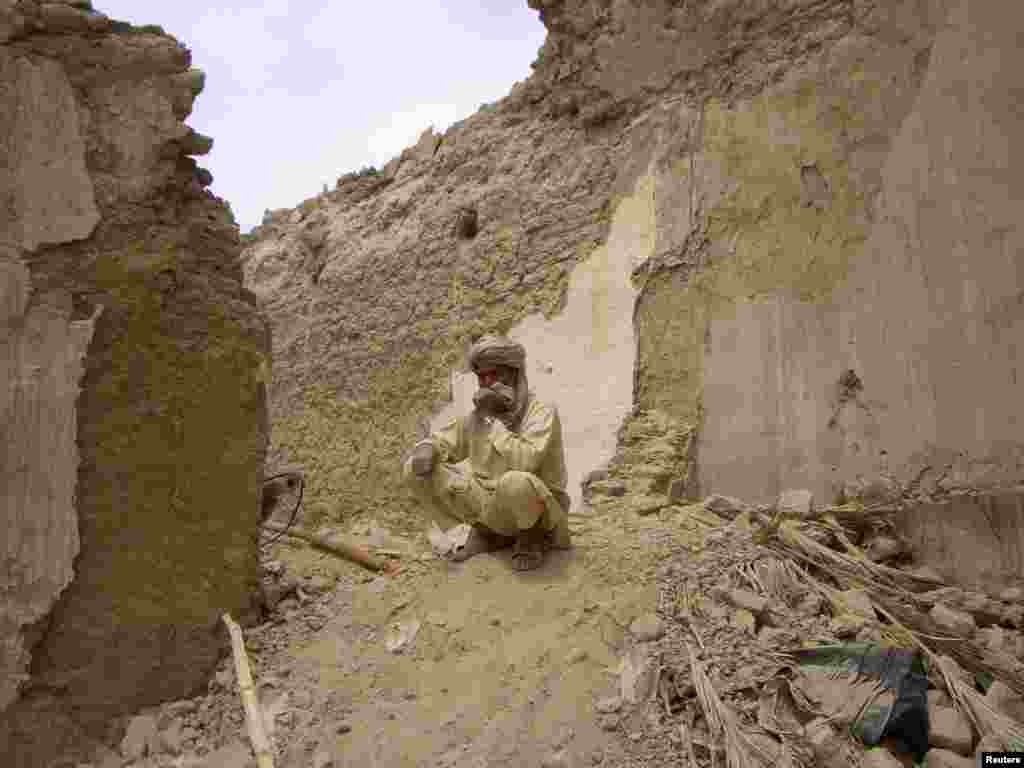 Seorang warga yang selamat dari gempa, duduk di reruntuhan rumahnya yang terbuat dari tanah di kota Mashkeel, provinsi Baluchistan, Pakistan, dekat perbatasan Iran.