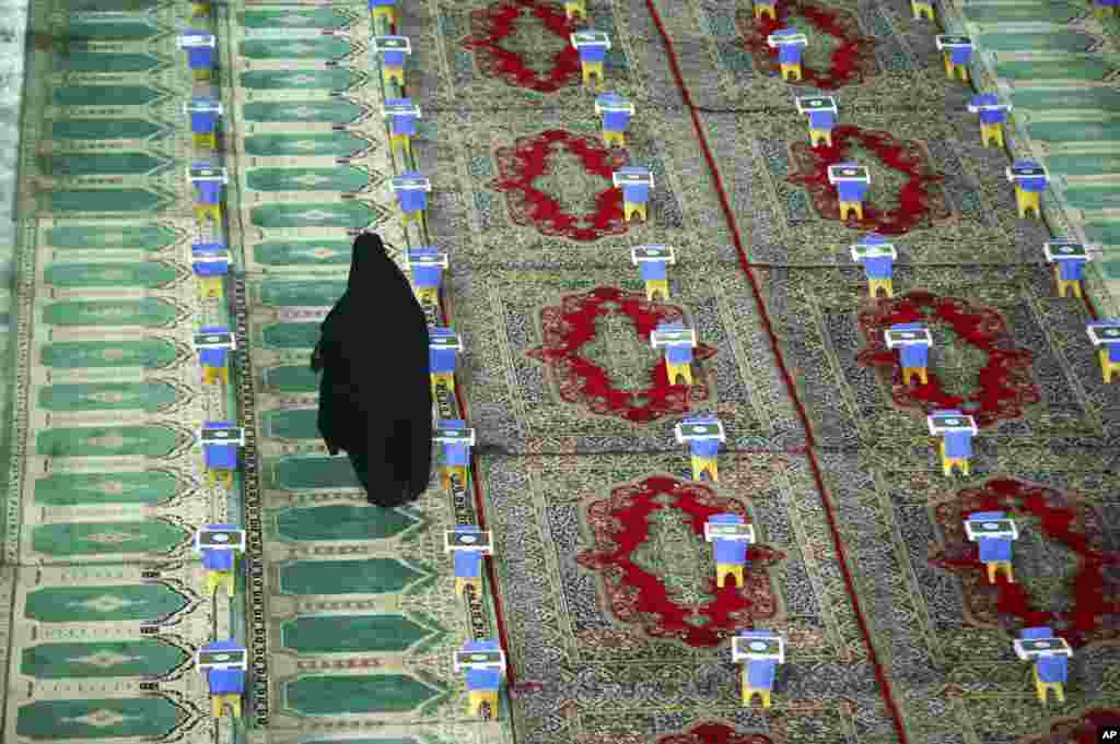Seorang perempuan Iran berjalan diantara salinan Alquran, Kitab Suci umat Islam, yang disiapkan untuk upacara selama bulan Ramadhan di Masjid Mohammad Ali Ibnu Helal di kota Aran dan Bidgol, sekitar 140 mil (225 kilometer) di selatan Teheran. 