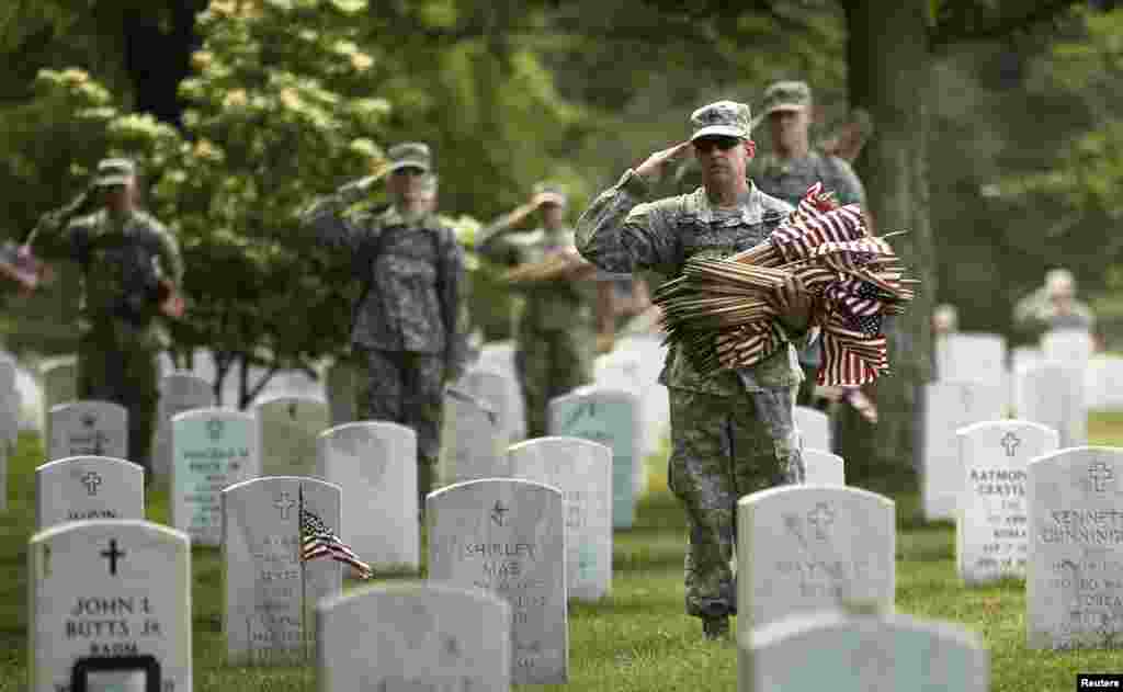 Para tentara memberikan penghormatan saat terdengar bunyi alunan terompet mengiringi sebuah pemakaman militer di dekatnya, saat mereka menaruh bendera di makam-makam di Taman Makam Pahlawan Nasional di Arlington, Virginia, 24 Mei 2013.