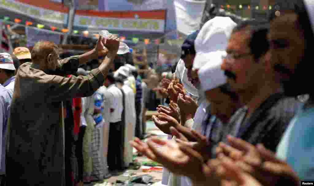 Seorang anggota gerakan Ikhwanul Muslimin dan pendukung Mohamed Morsi menyiramkan air untuk mendinginkan orang-orang selama shalat di berjamaah di lapangan Rabaa Adawiya di Kairo (15/7). (Reuters/Amr Abdallah Dalsh)