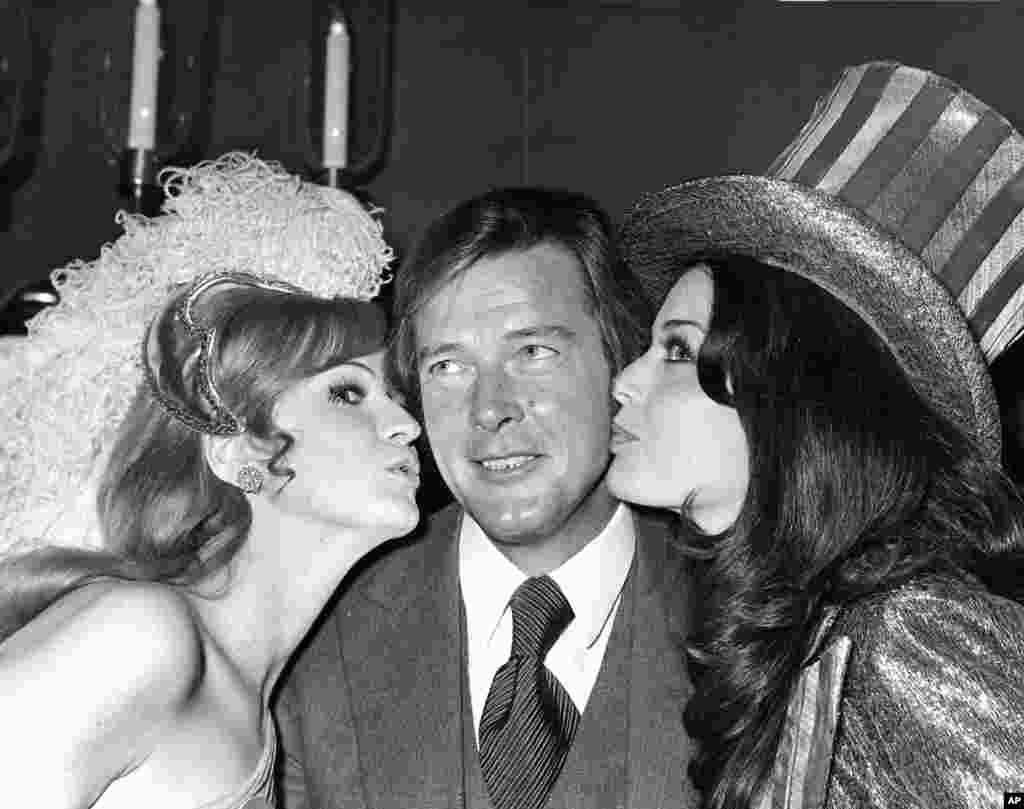 影星罗杰·摩尔1971年在世界小姐选美的午餐会上接受英国小姐和美国小姐的亲吻。 罗杰·摩尔的家人2017年5月23日说,他在和癌症短期搏斗后去世。 
