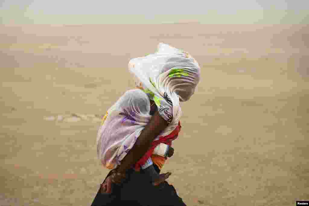 A woman carrying her baby and wrapped with a shawl walks through a sandstorm in Timbuktu, Mali, July 29, 2013.