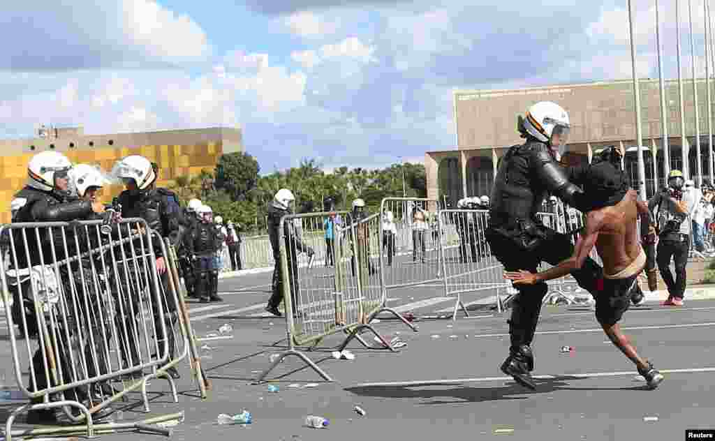 Seorang demonstran bentrok dengan polisi anti huru-hara dalam protes menentang Presiden Michel Temer dan skandal korupsi pemerintah di Brasilia, Brazil.