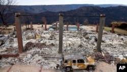 FILE - A vehicle rests in front of a home leveled by the Camp Fire in Paradise, Calif., Dec. 3, 2018. Authorities estimate it will cost at least $3 billion to clear debris of 19,000 homes destroyed by California wildfires last month.