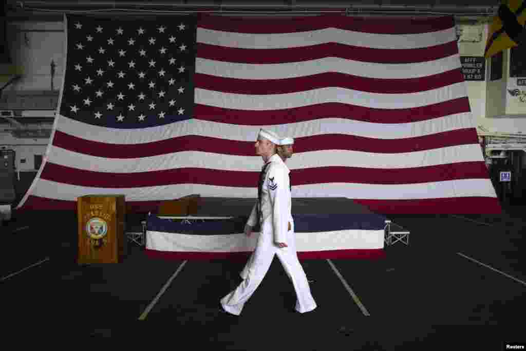 2013年4月15日,美国两栖攻击舰貝里琉号(USS Peleliu)上的美国国旗前面,两位水兵走过。当时正在香港进行例行港口访问的貝里琉号停泊在尖沙咀。