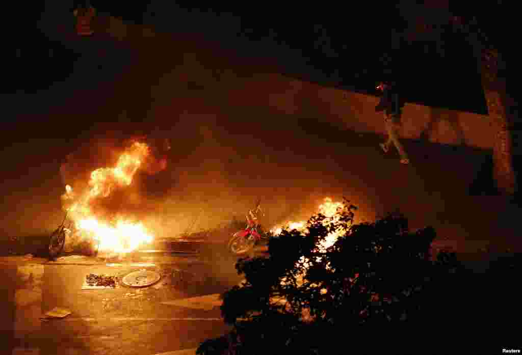 A motorcycle taxi driver walks past burning motorcycles set ablaze by anti-government demonstrators at Altamira Square in Caracas, Feb. 26, 2014. 