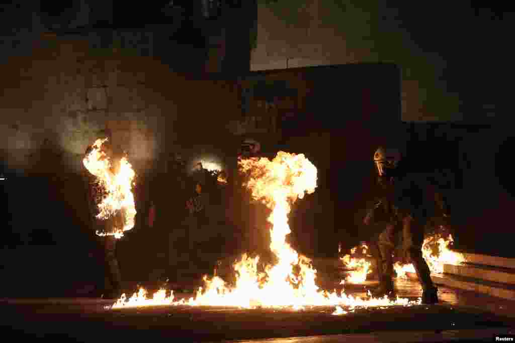 Seorang demonstran bertopeng melemparkan bom molotov ke arah polisi anti huru-hara di luar gedung parlemen di Athena, saat anggota parlemen Yunani melakukan voting 'program penghematan'.