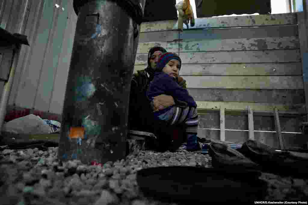 Syrian mother holds her grandson close to the stove in front of their closed container house in the refugee camp in Harmanli. UNHCR/D.Kashavelov