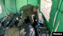Ritual worker picks up bodies of killed Russian soldiers to load them to refrigerated rail car, in Kharkiv