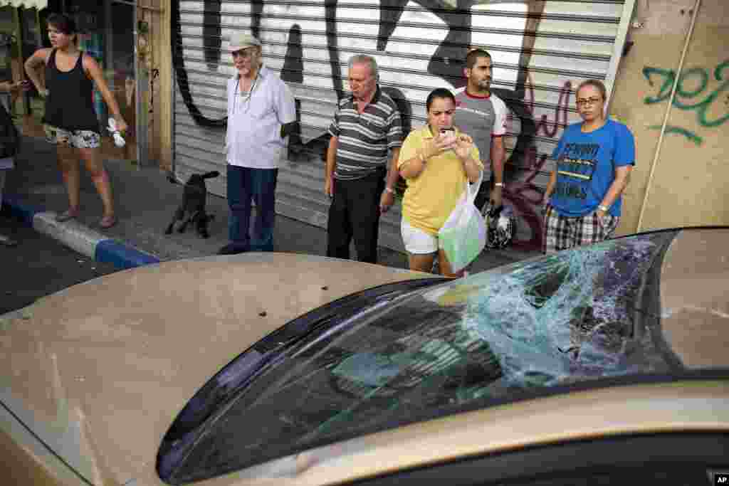 Warga Israel melihat-lihat mobil yang rusak oleh sisa-sisa roket jarak jauh yang ditembakkan oleh militan Palestina dari Gaza yang ditembak jatuh oleh Israel, di Tel Aviv (10/7). (AP/Oded Balilty)